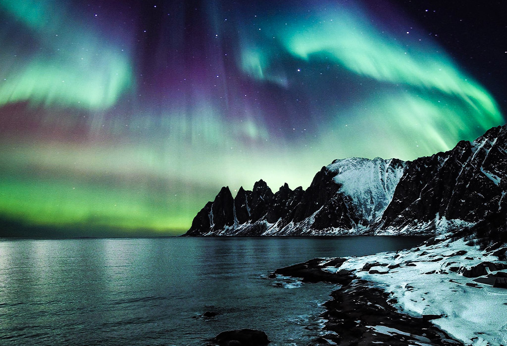 view of the northern lights beside mountains and water
