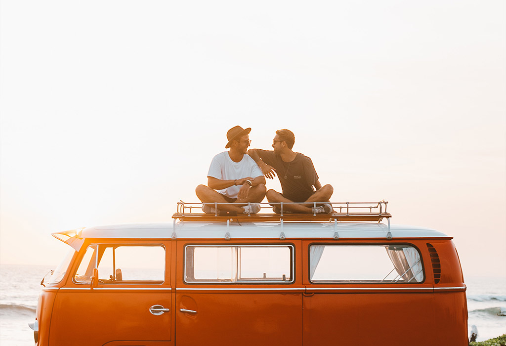 two men sitting on top of a van laughing at sunset